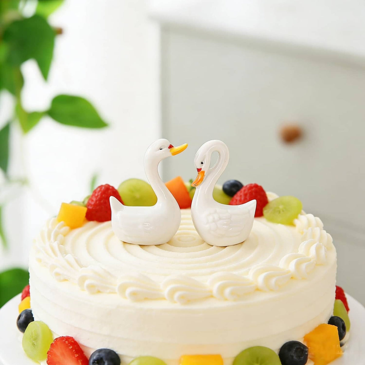 Two small white ceramic swan cake toppers on a frosted celebration cake