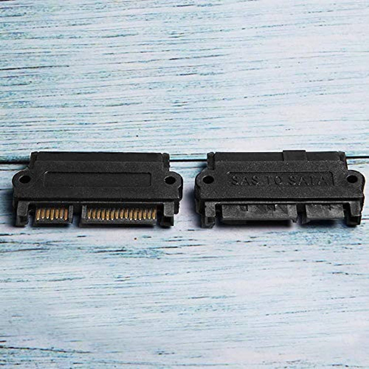 SAS to SATA adapter pair on wood, black housings with exposed gold pin arrays