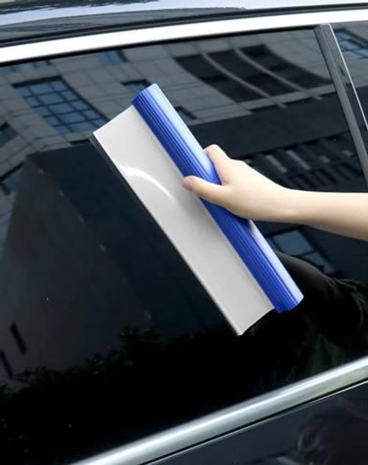 Hand holding blue car squeegee with white blade against a car window