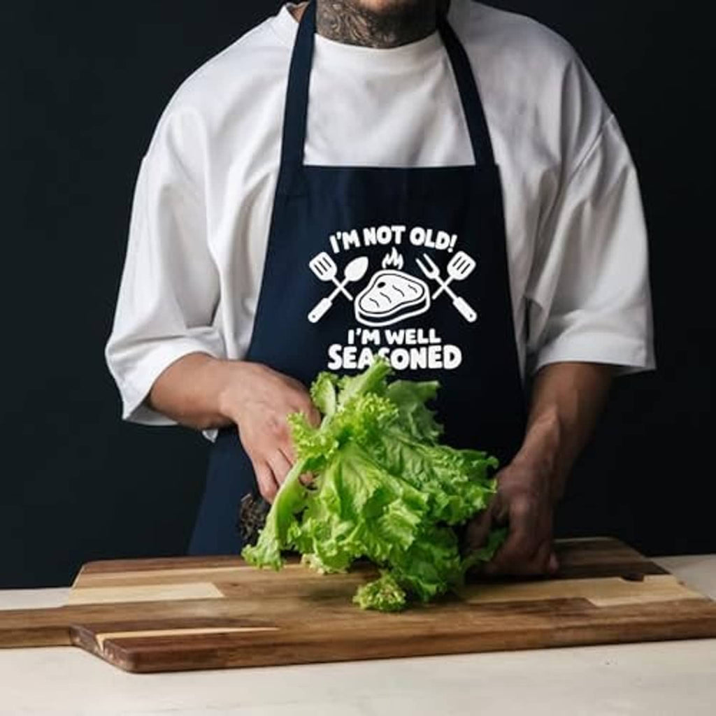 Black cooking apron with "I'm well seasoned" graphic, worn over a white chef shirt