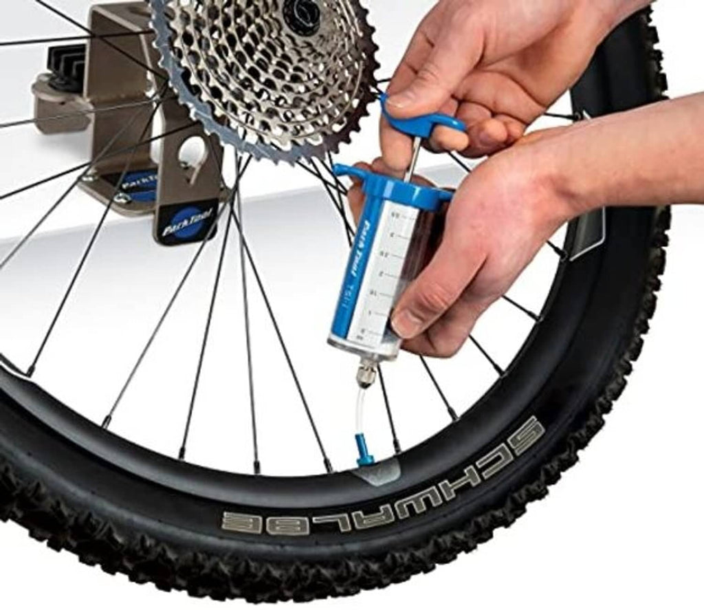 Hands applying blue tubeless sealant injector to rear wheel rim and valve