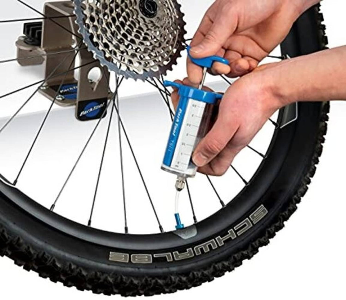 Hands applying blue tubeless sealant injector to rear wheel rim and valve