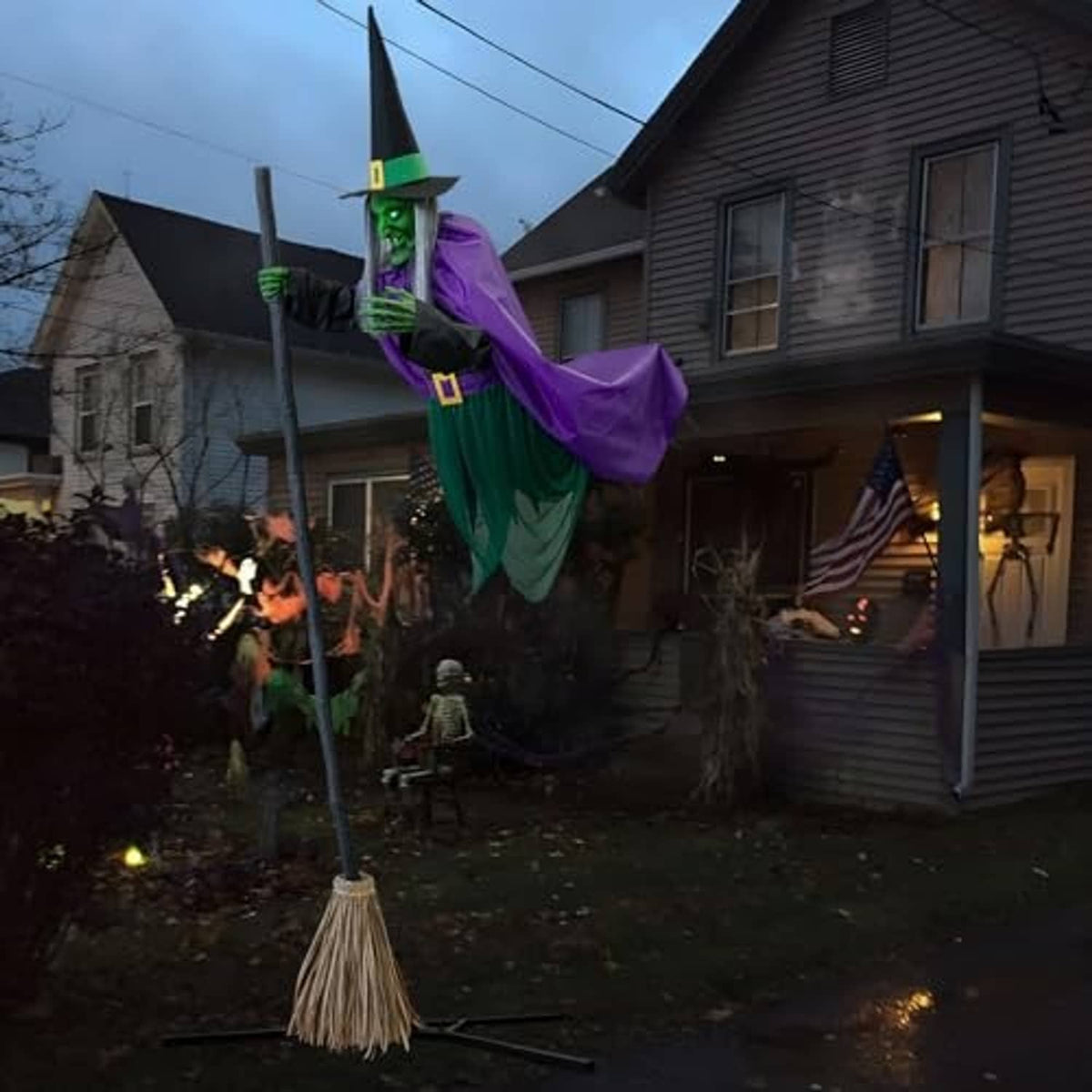 Outdoor animated witch yard decoration with glowing green face, purple robe, and broom base