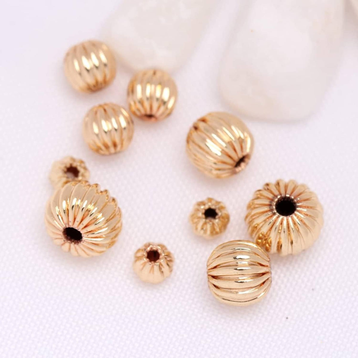 Gold-tone ribbed round beads with black center dots, scattered on white