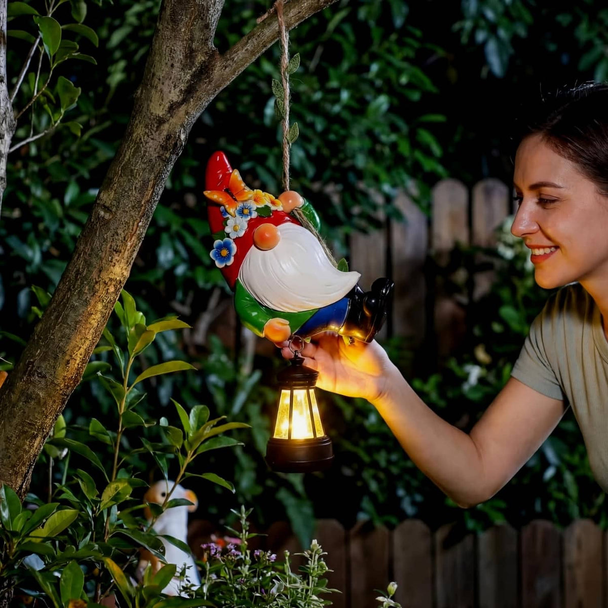 Solar hanging gnome statue with white beard and glowing lantern in a garden