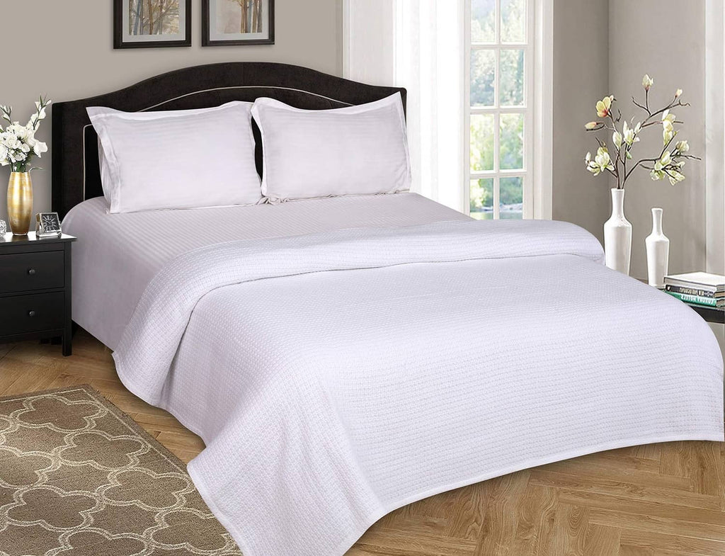 White bed blanket with waffle weave draped over full-size bed.