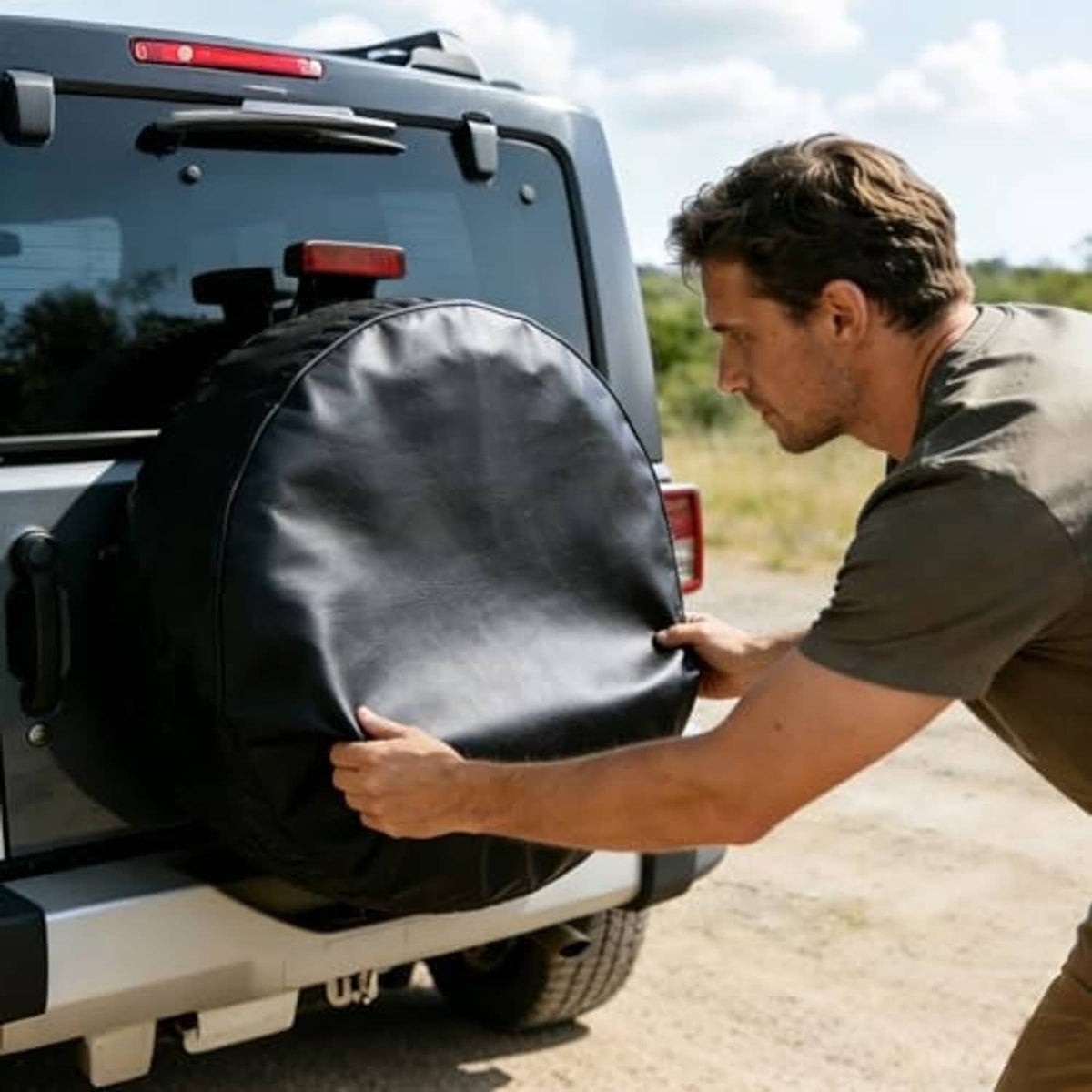 Black spare tire cover installation on vehicle rear, round cover held by hands