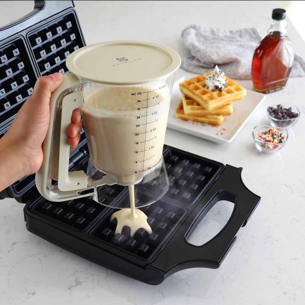 Beige batter dispenser pouring batter onto waffle maker grid