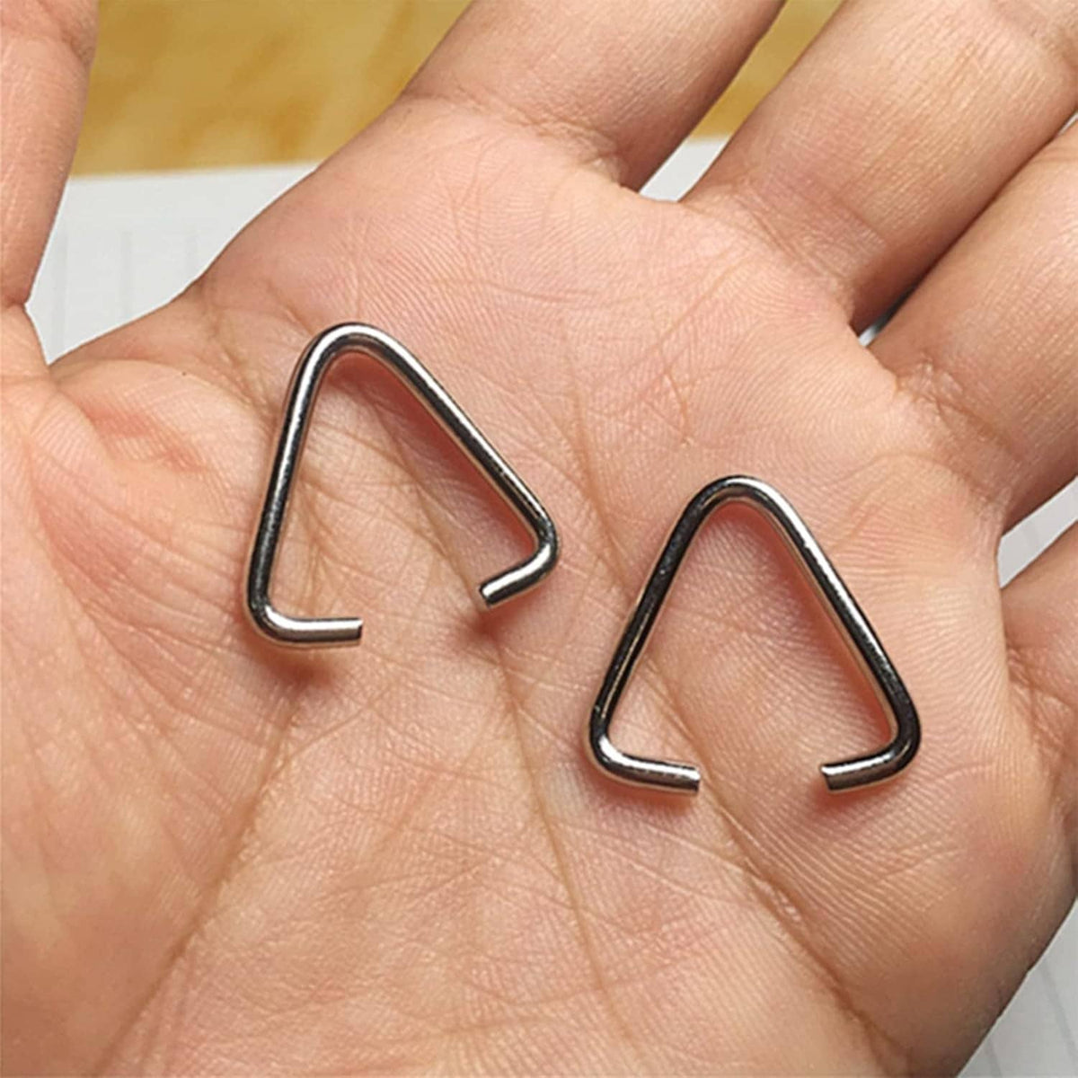 Triangle open jump rings held in hand, silver-tone metal pinch-bail clip connectors