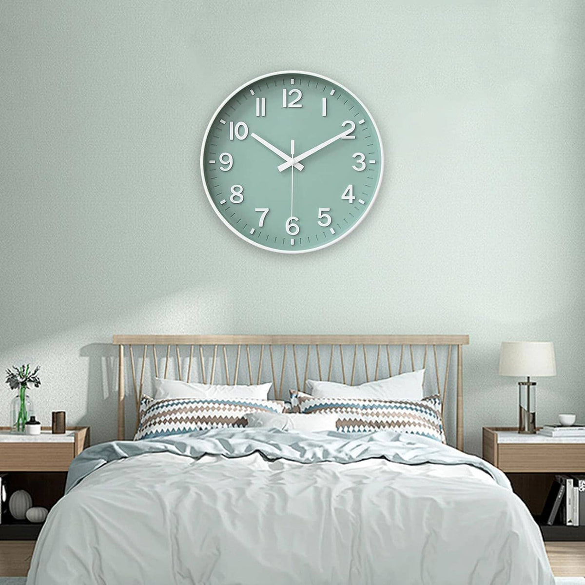 Small green round wall clock with white hands and numerals hanging above a bed.