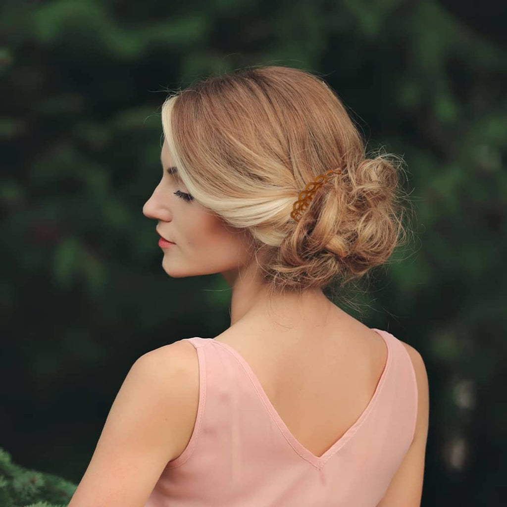 Plastic hair side comb with amber teeth, holding a blonde updo