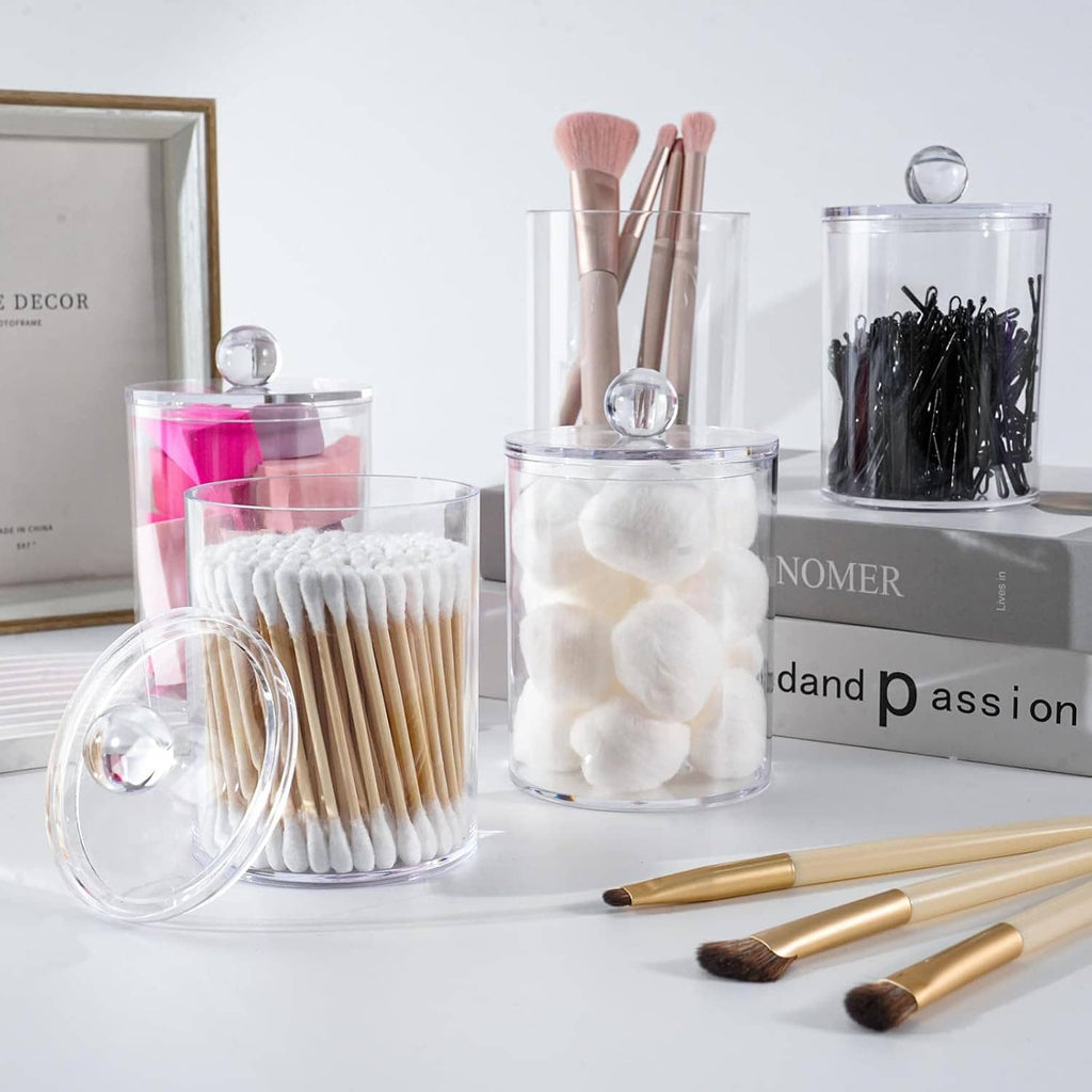 Clear apothecary jars with lids holding pink, white, and black cotton swabs on vanity