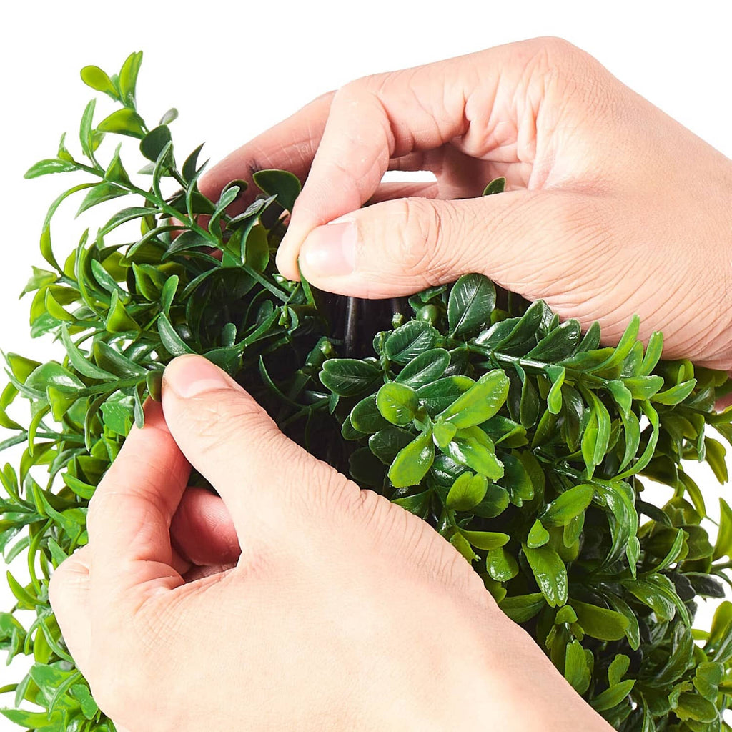 Artificial boxwood topiary tree leaves being shaped by hands, bright green foliage