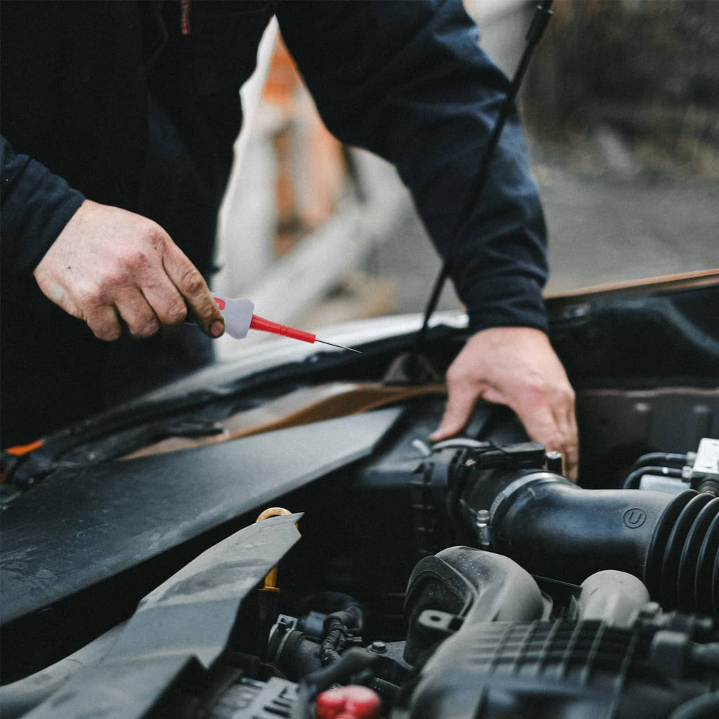 Automotive technician using a red-handled terminal removal tool on a car