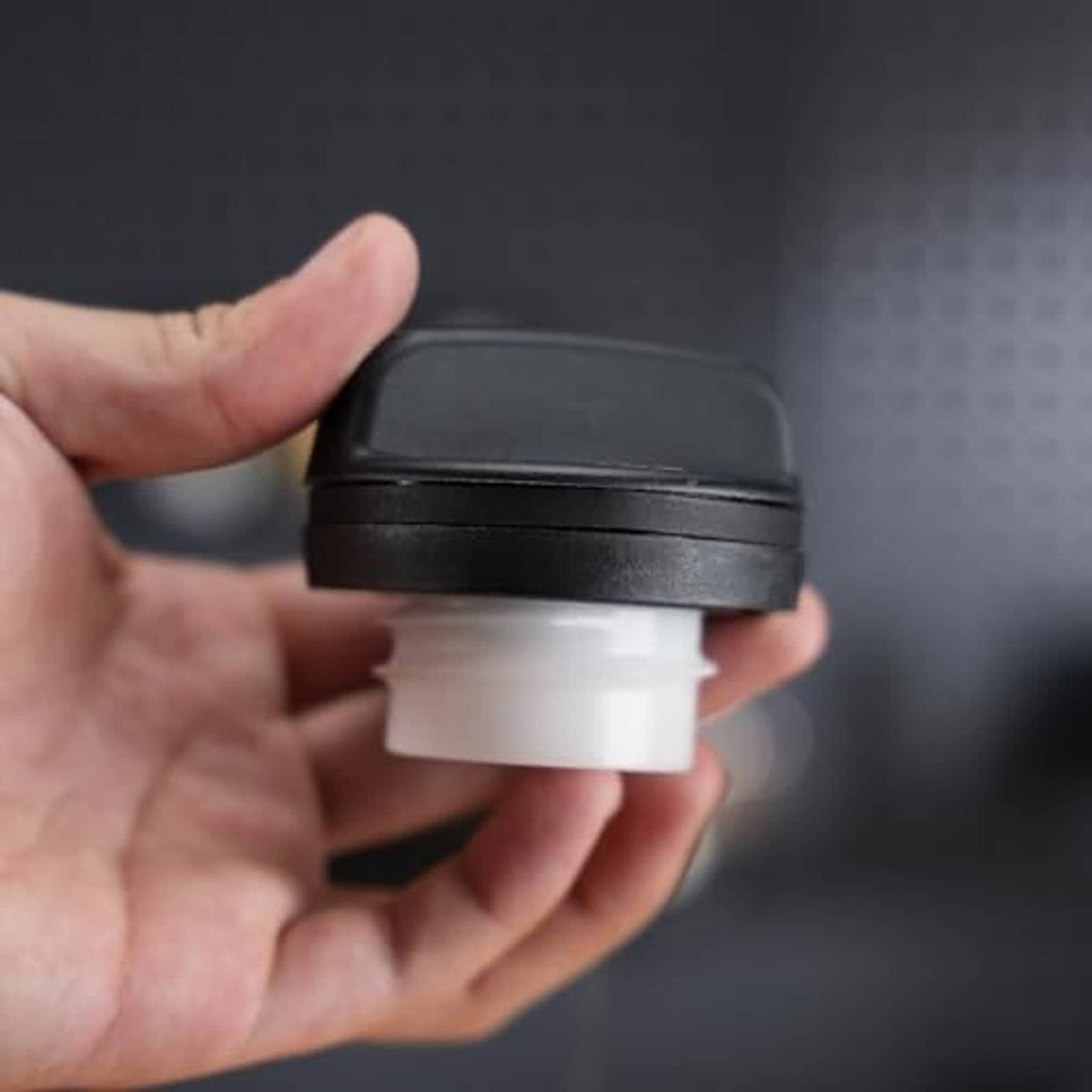 Fuel tank filler cap side view in hand, black housing with white inner ring.