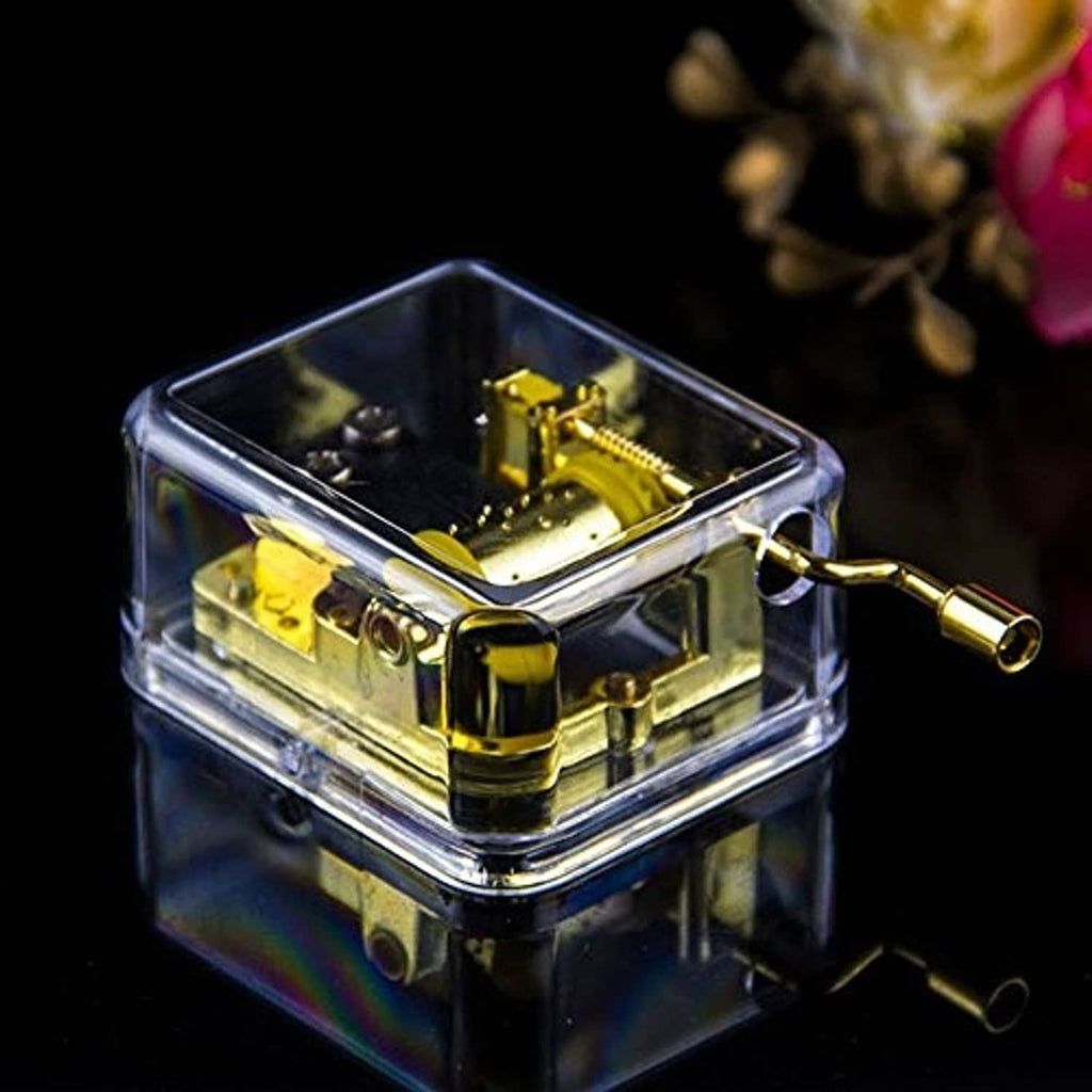 Transparent clear music box with gold hand-crank mechanism and crank handle on the side.