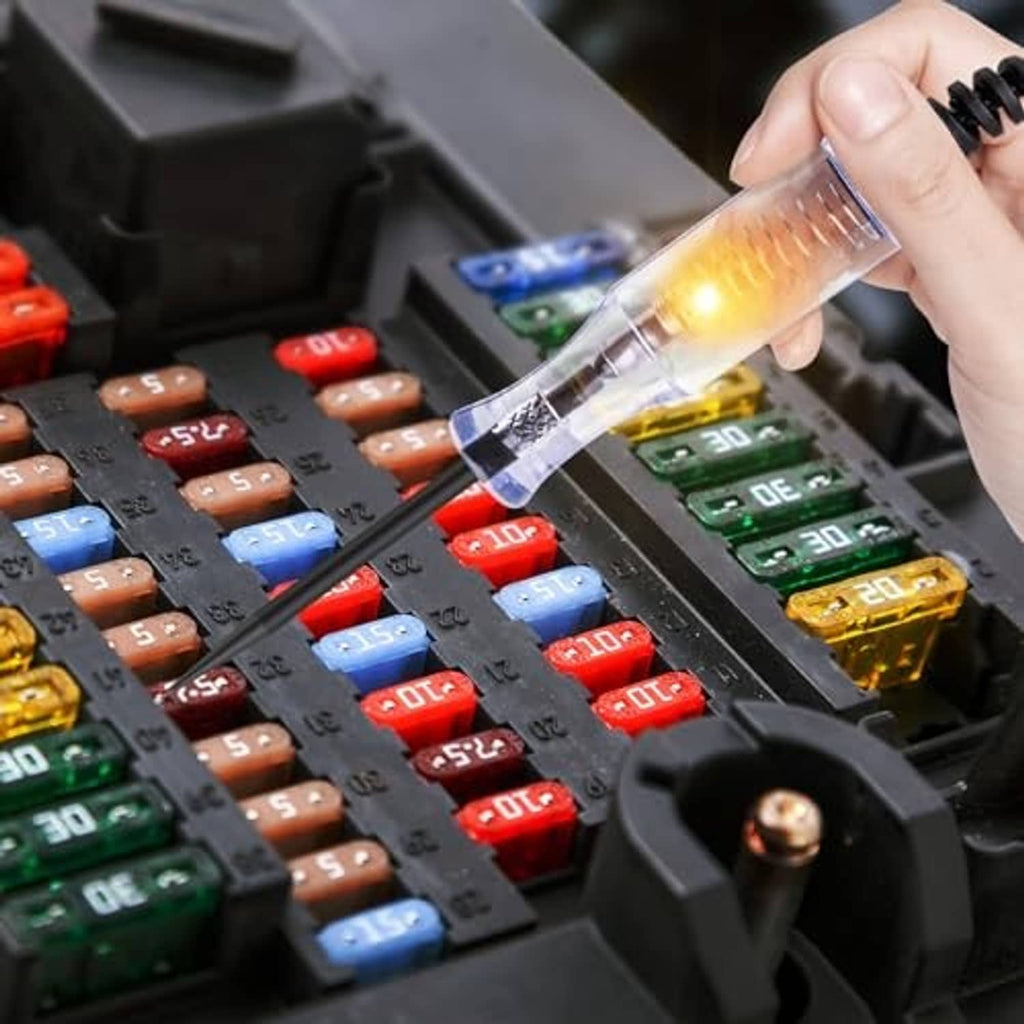 Glowing DC circuit tester probe held over fuse block with multiple colored fuses