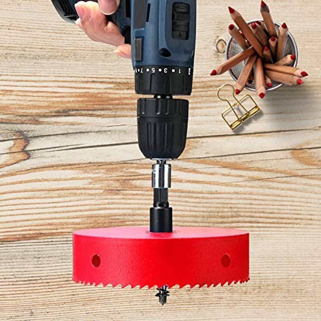Red bi-metal hole saw mounted on a drill, cutting into a wooden board.