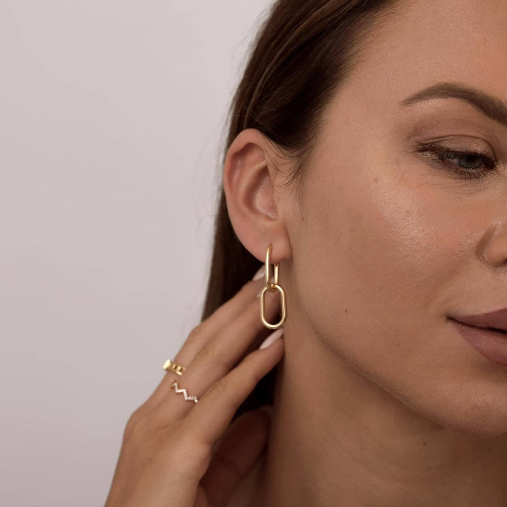 Gold paperclip huggie hoop earrings on ear, polished rectangular loops