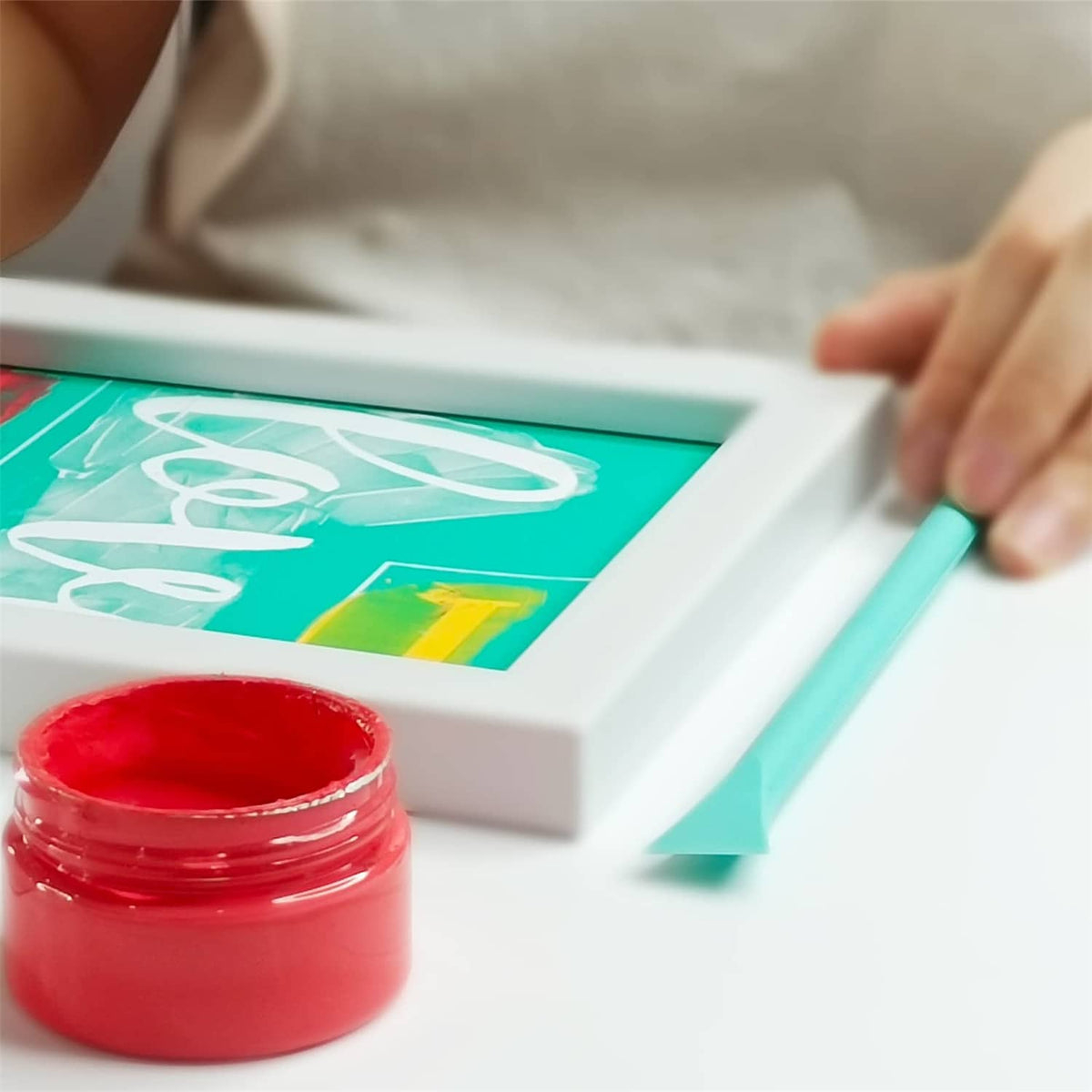 Red chalk paste ink jar with teal ink on a screen printing stencil