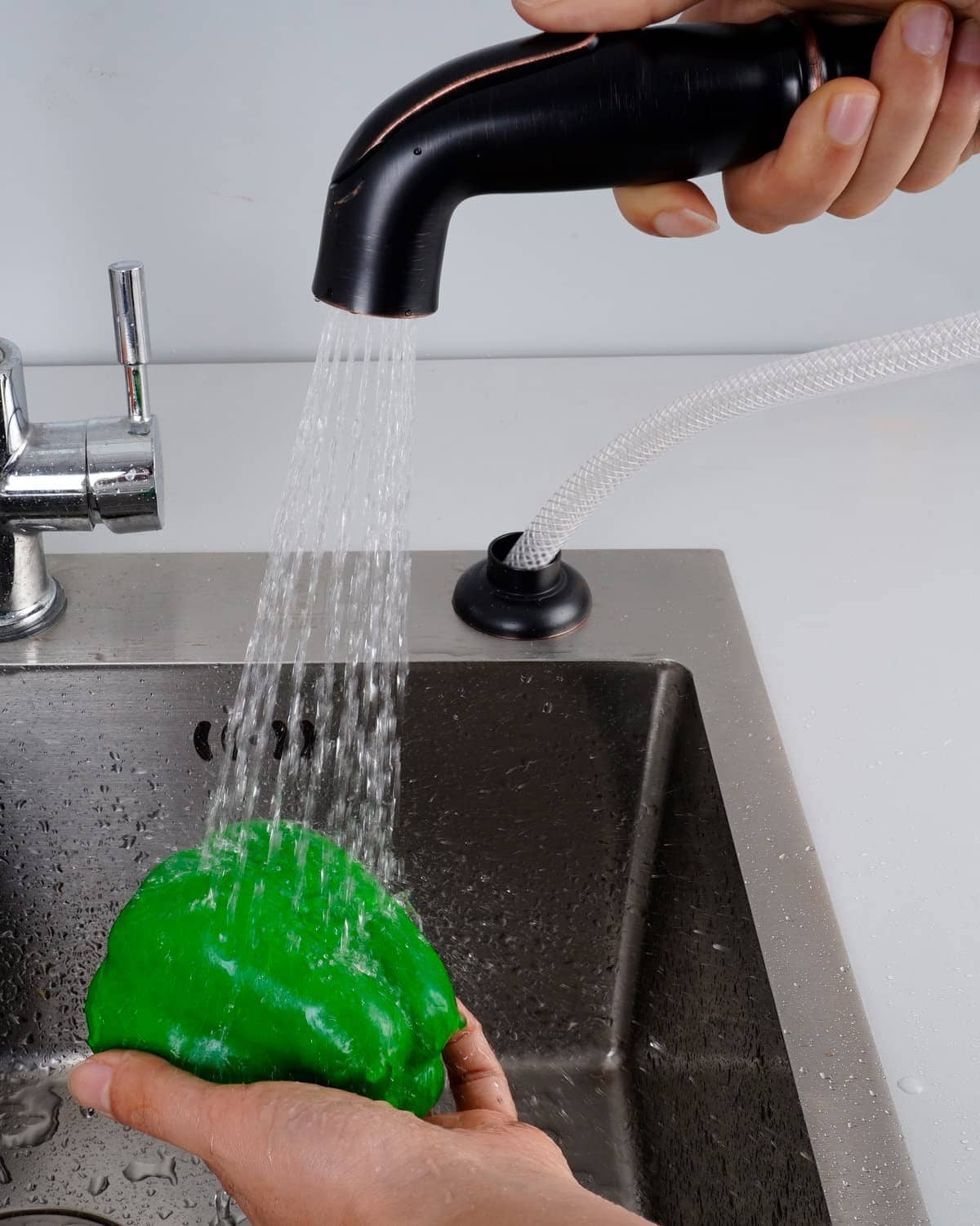 Black sink sprayer head releasing a water stream from braided hose into kitchen sink