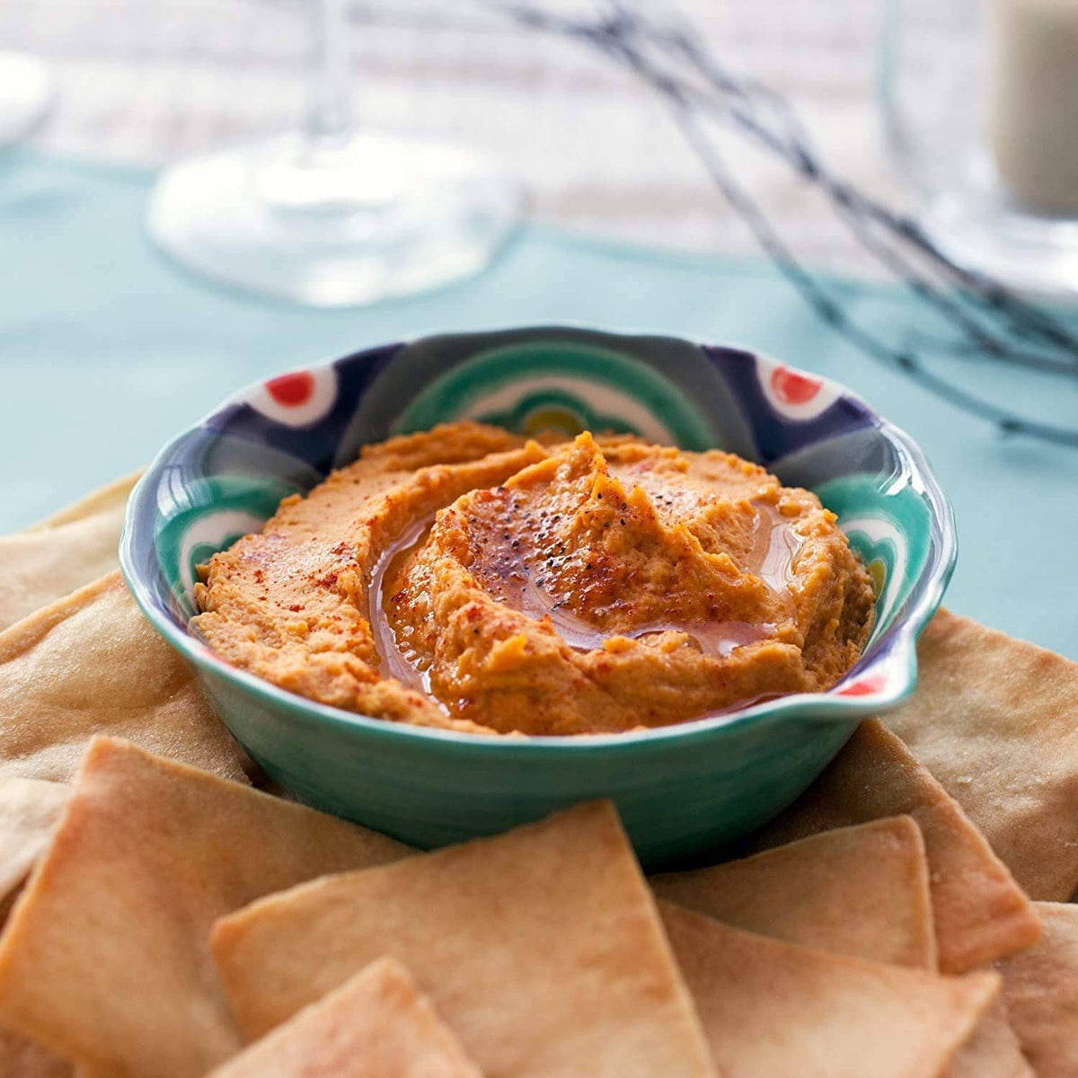 Baked pita chips with creamy orange dip in a blue-green bowl