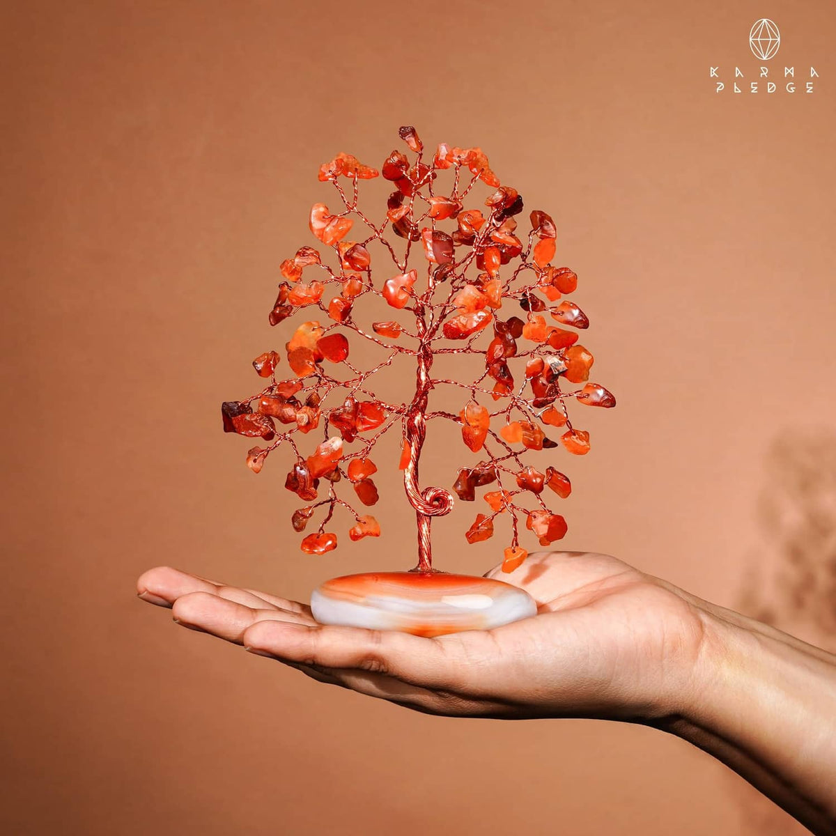 Carnelian crystal tree held in hand, orange-red stones on white palm-stone base