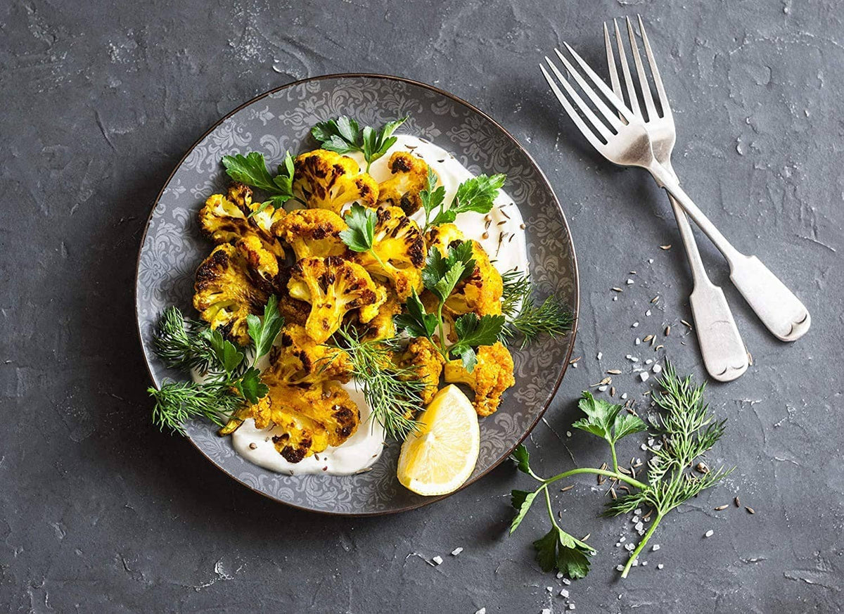 Turmeric-seasoned roasted dish on a plate with lemon wedge and herbs