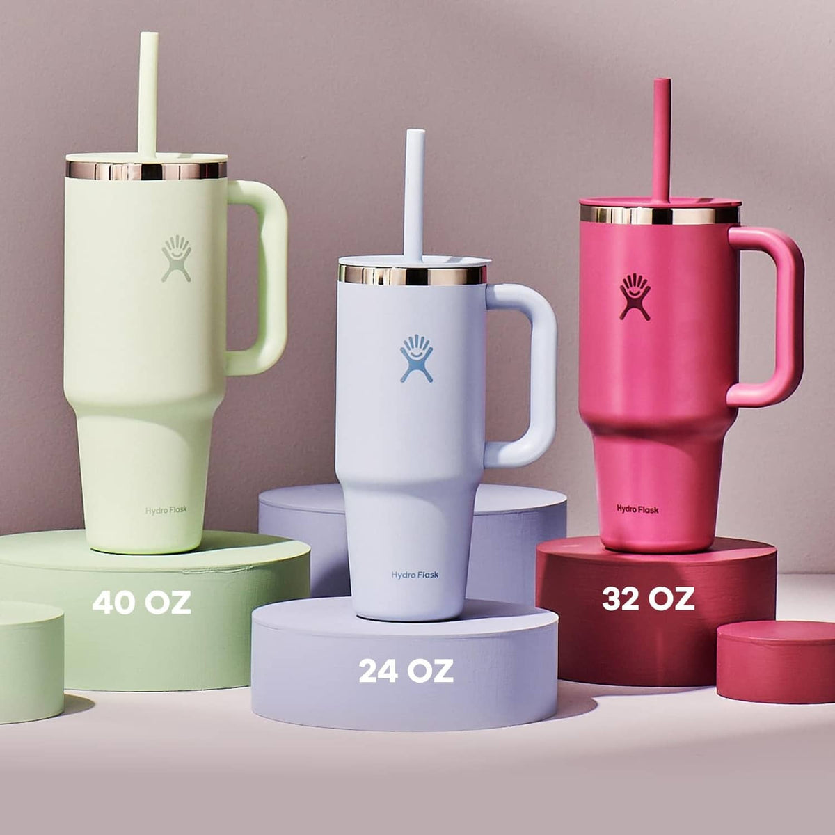 Set of travel tumblers with handles and straws in light green, blue, and pink.