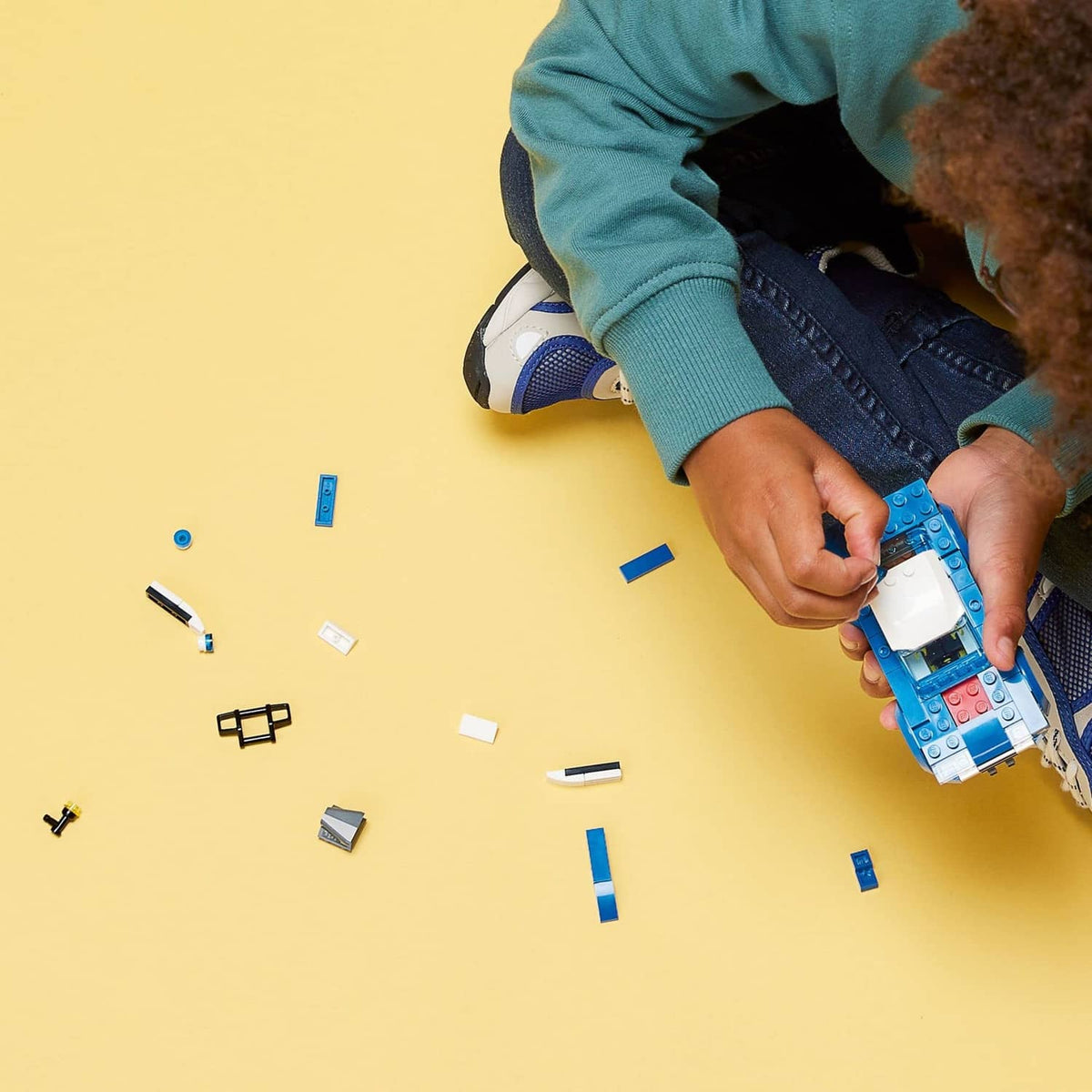 Child building a blue police toy car with small multicolor pieces