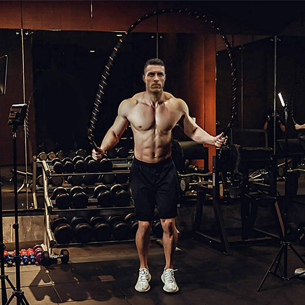 Man holding a black weighted jump rope with orange-accented braided handles in gym.