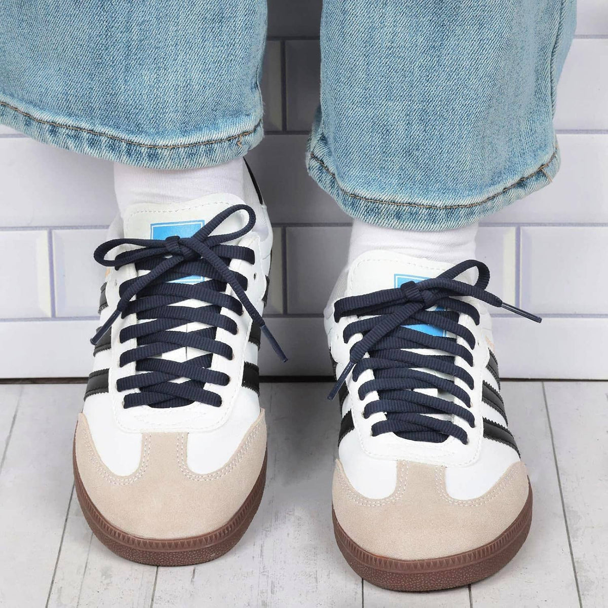 Black flat shoelaces tied on white and beige sneakers with eyelets