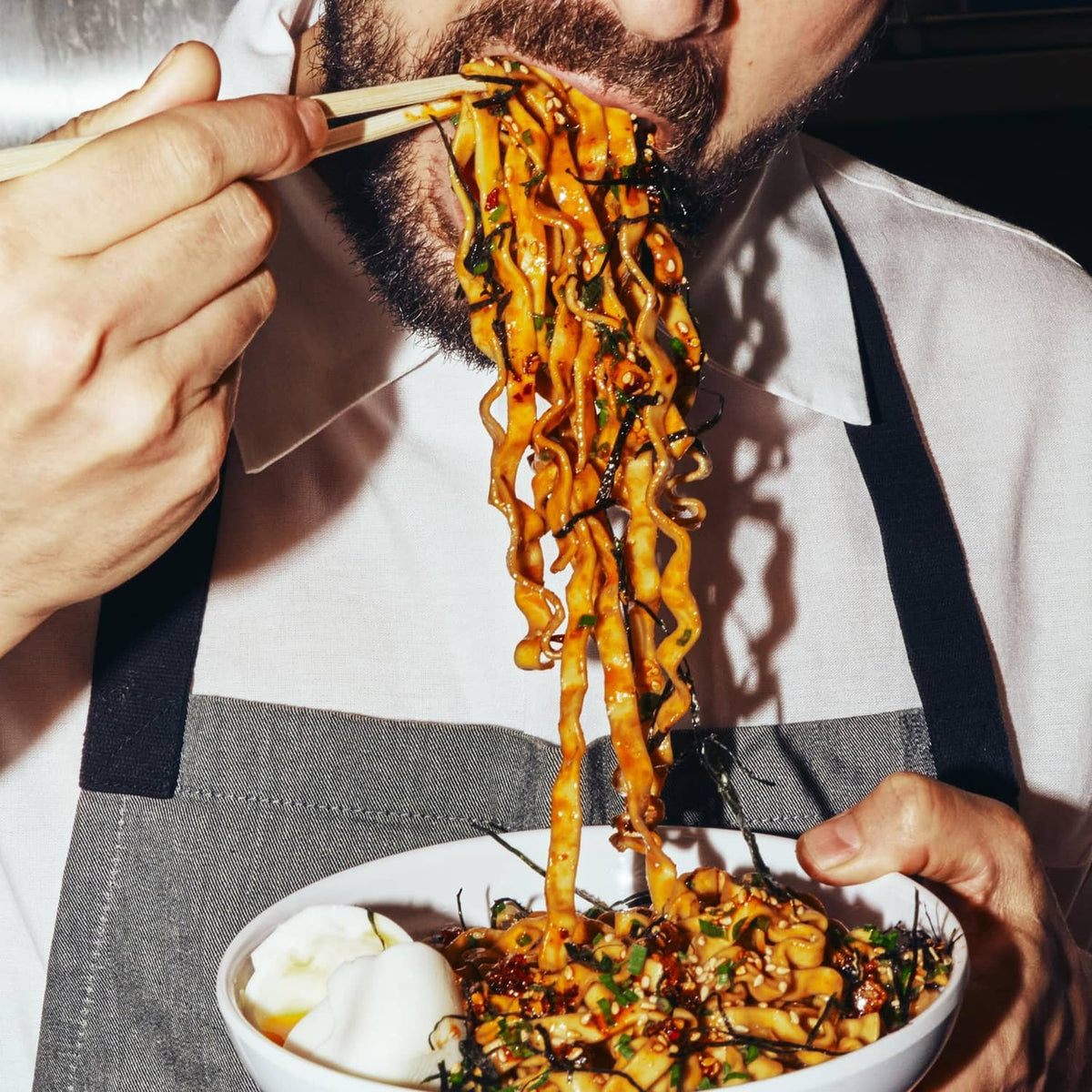 Tingly chili ramen noodles lifted with chopsticks above a bowl of sauce