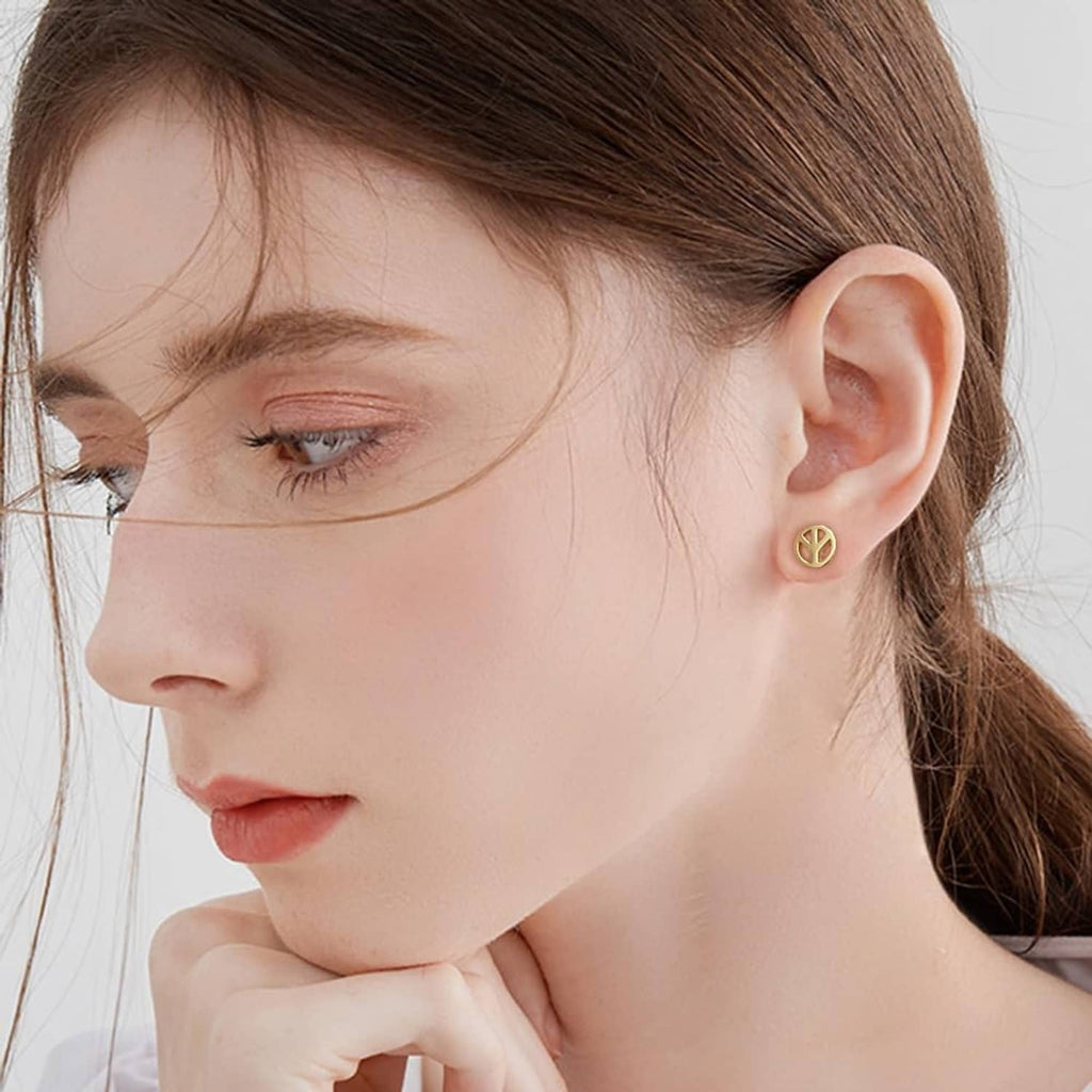 Gold-tone peace sign stud earring on ear with round disc and small black backing