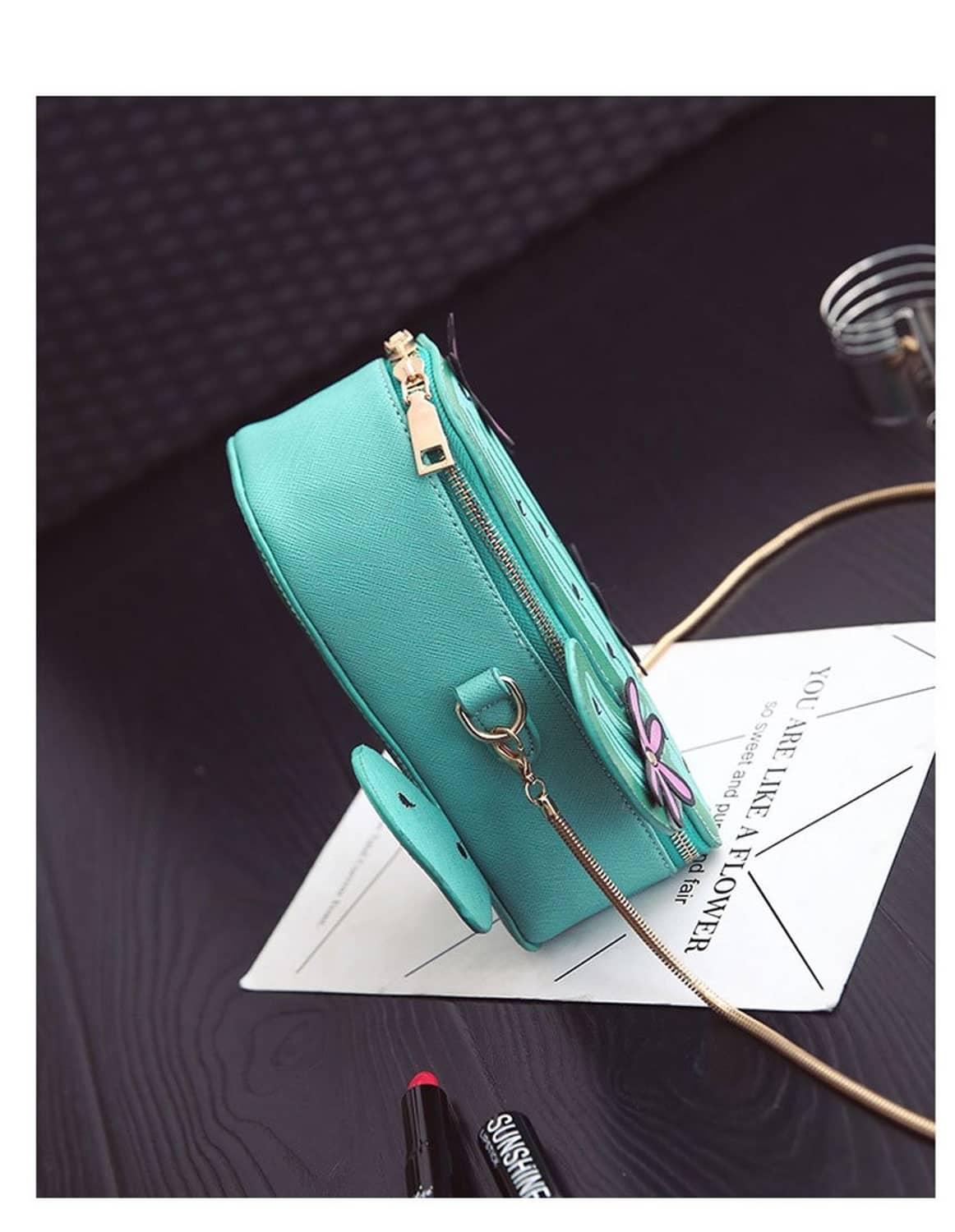 Teal cactus-shaped mini crossbody bag with gold zipper, chain strap, and purple flower charm