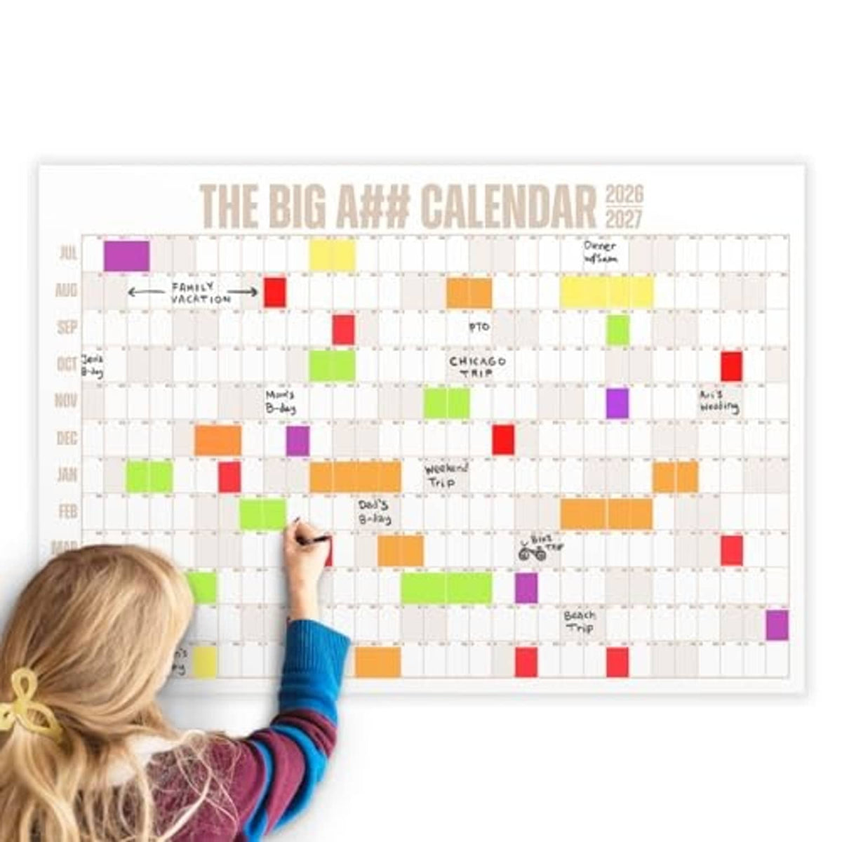 Dry-erase wall calendar grid with colored blocks and labels, person writing in the month layout