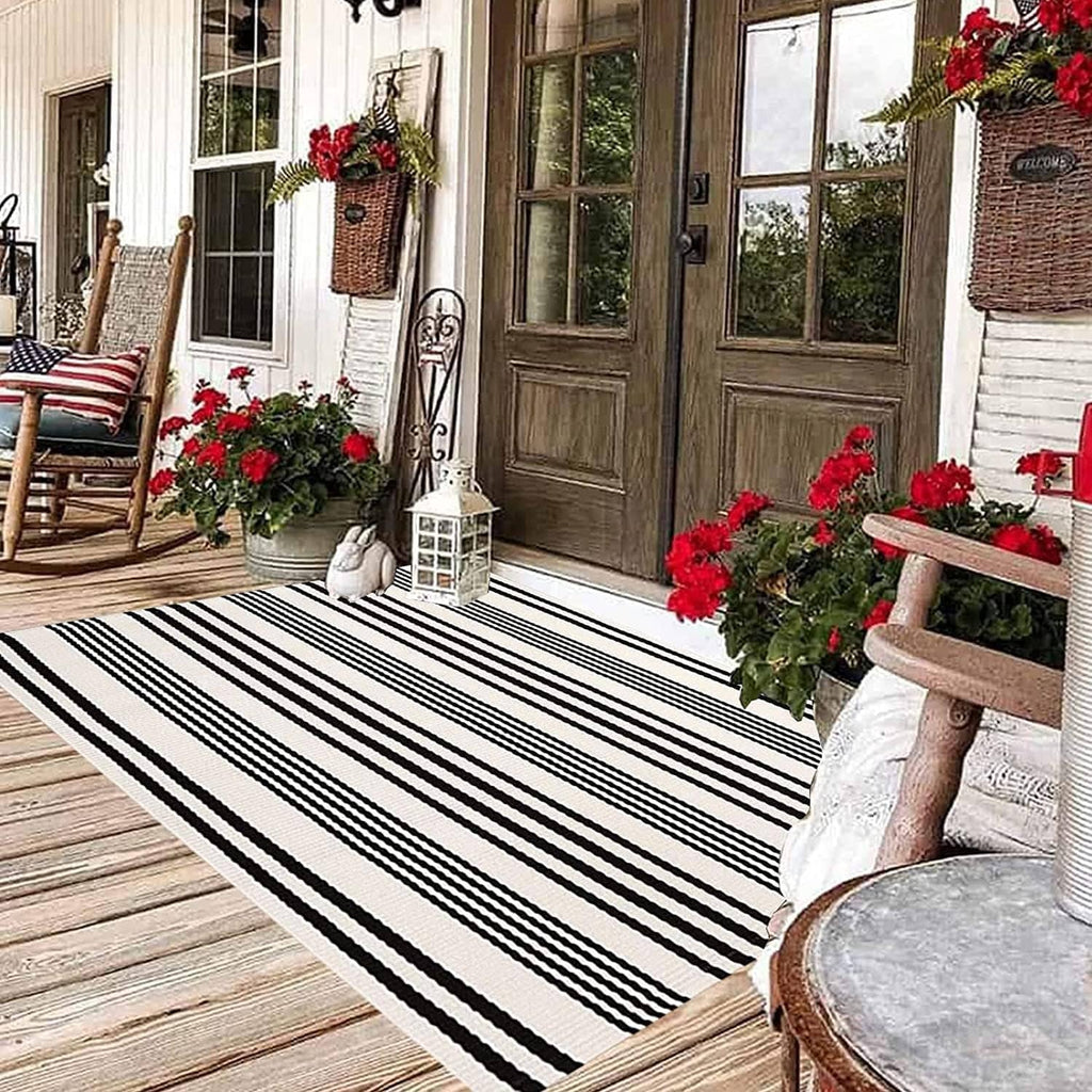 Black-and-white striped outdoor rug laid on a wood deck, rectangular with horizontal bands.