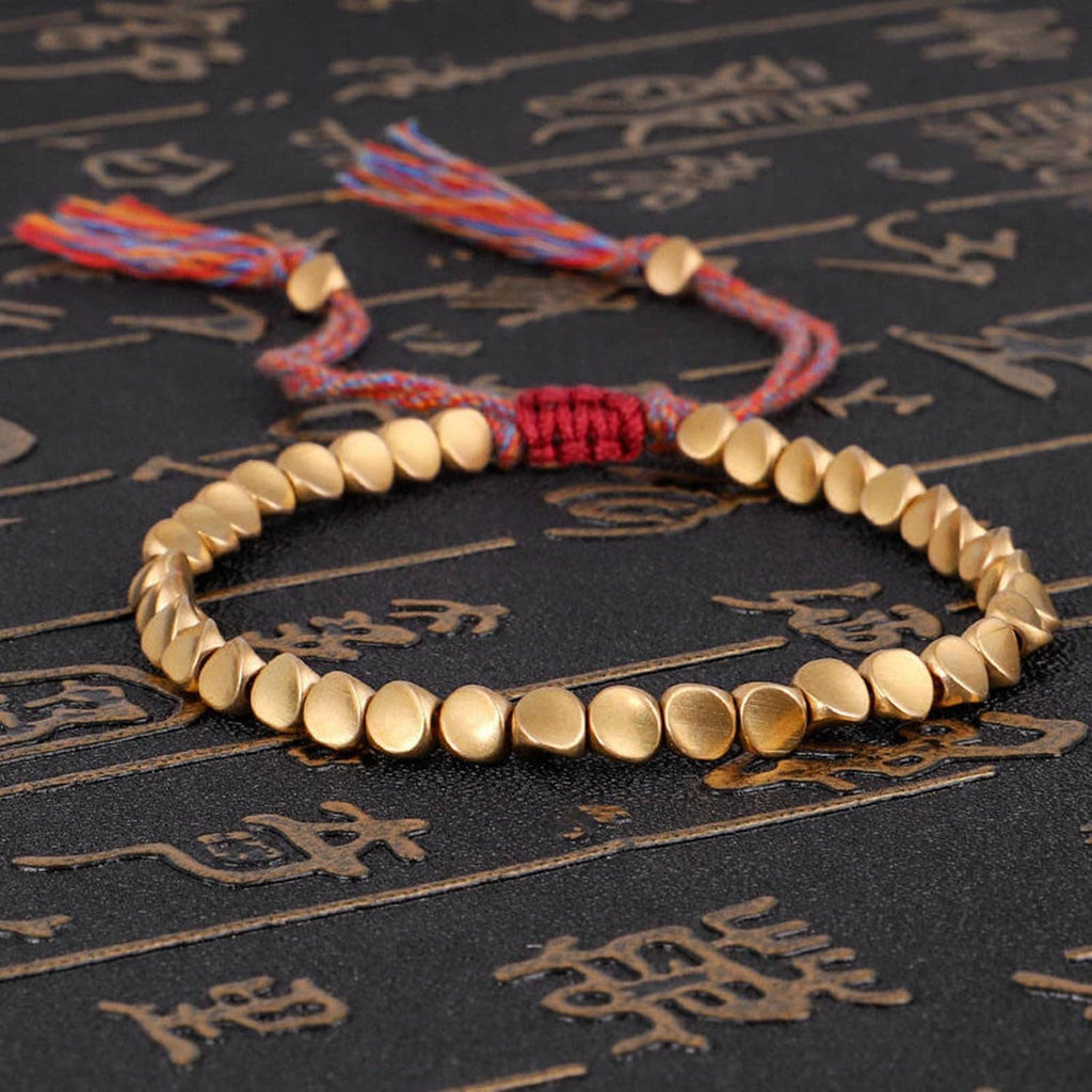 Gold-tone beaded bracelet with red braided center resting on dark surface.