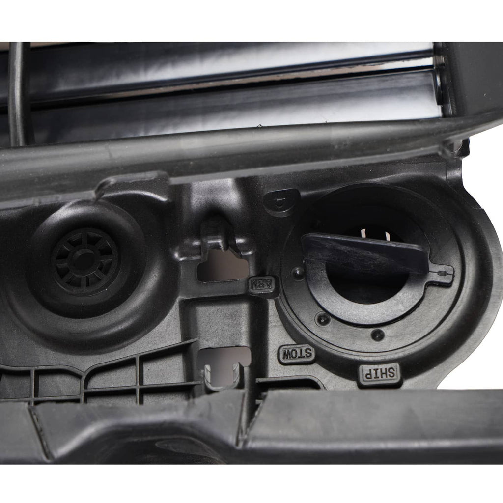 Close-up of black grille shutter motor area with circular cover and molded markings