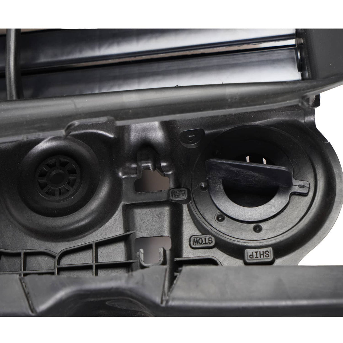 Close-up of black grille shutter motor area with circular cover and molded markings