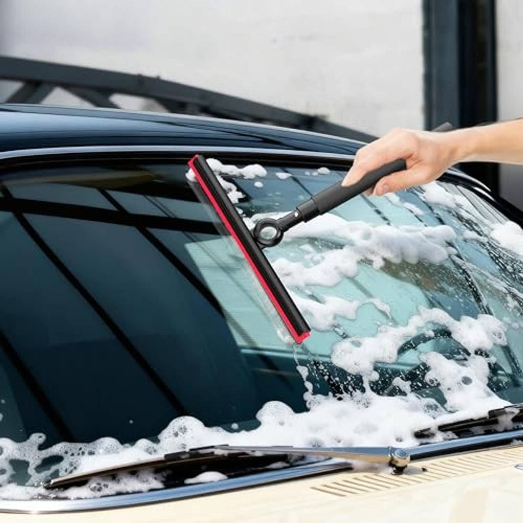 Automotive windshield squeegee with black handle and red-edged blade clearing soap suds