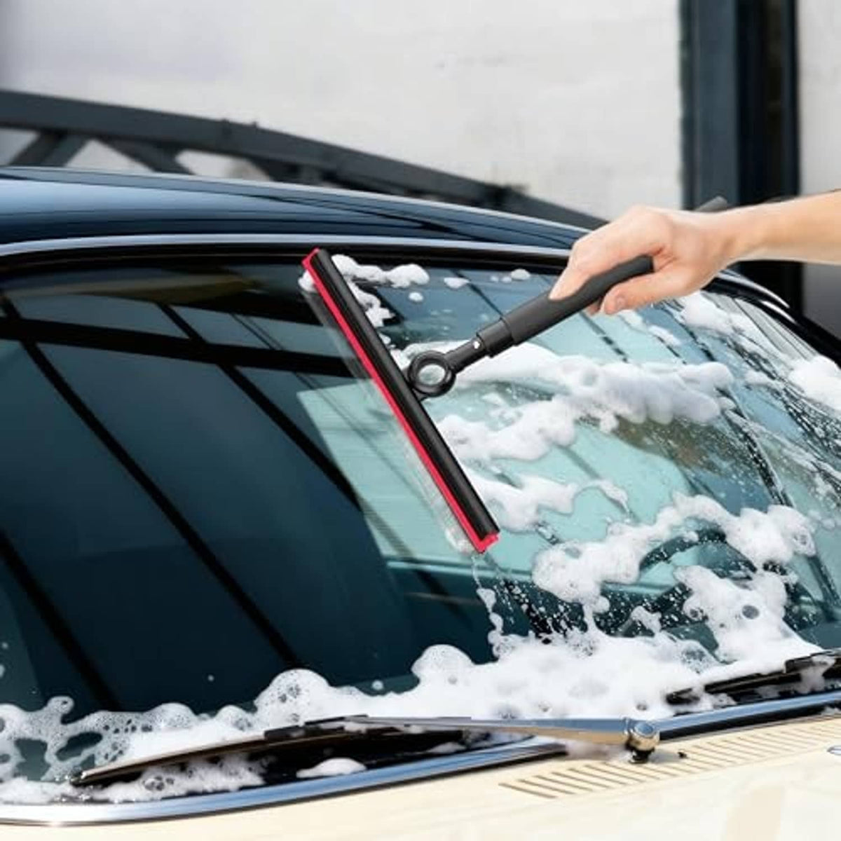 Automotive windshield squeegee with black handle and red-edged blade clearing soap suds
