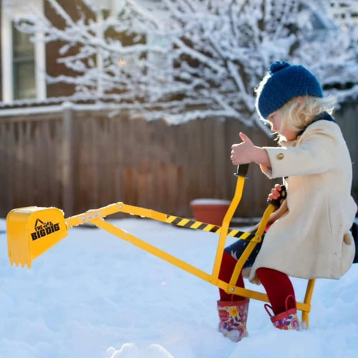 Yellow digger playset with digging arm and bucket, used by toddler in snow.