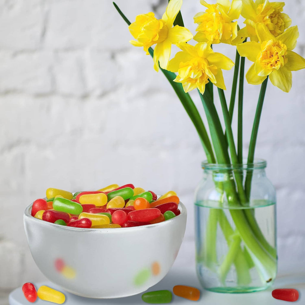 Bowl of assorted fruit candies beside a vase of yellow daffodils