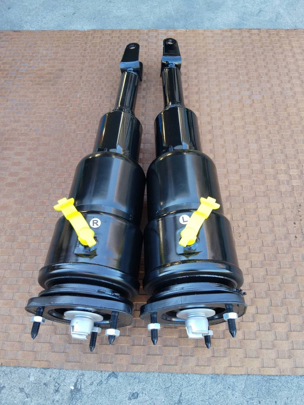 Two black air shock struts with mounting caps, yellow labels, and exposed lower bolts