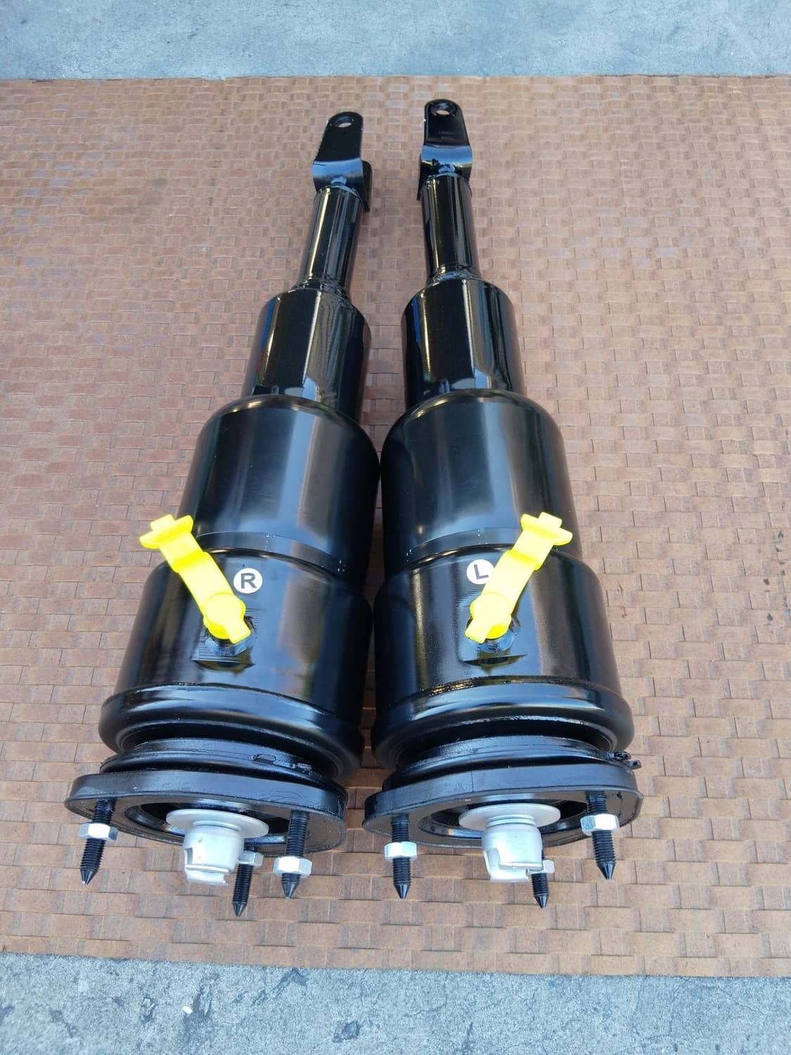 Two black air shock struts with mounting caps, yellow labels, and exposed lower bolts