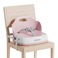 Pink baby booster seat with gray safety straps, sitting on a wooden chair