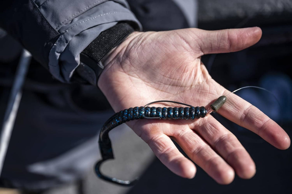Soft plastic curly-tail fishing worm, dark blue glitter body held in hand
