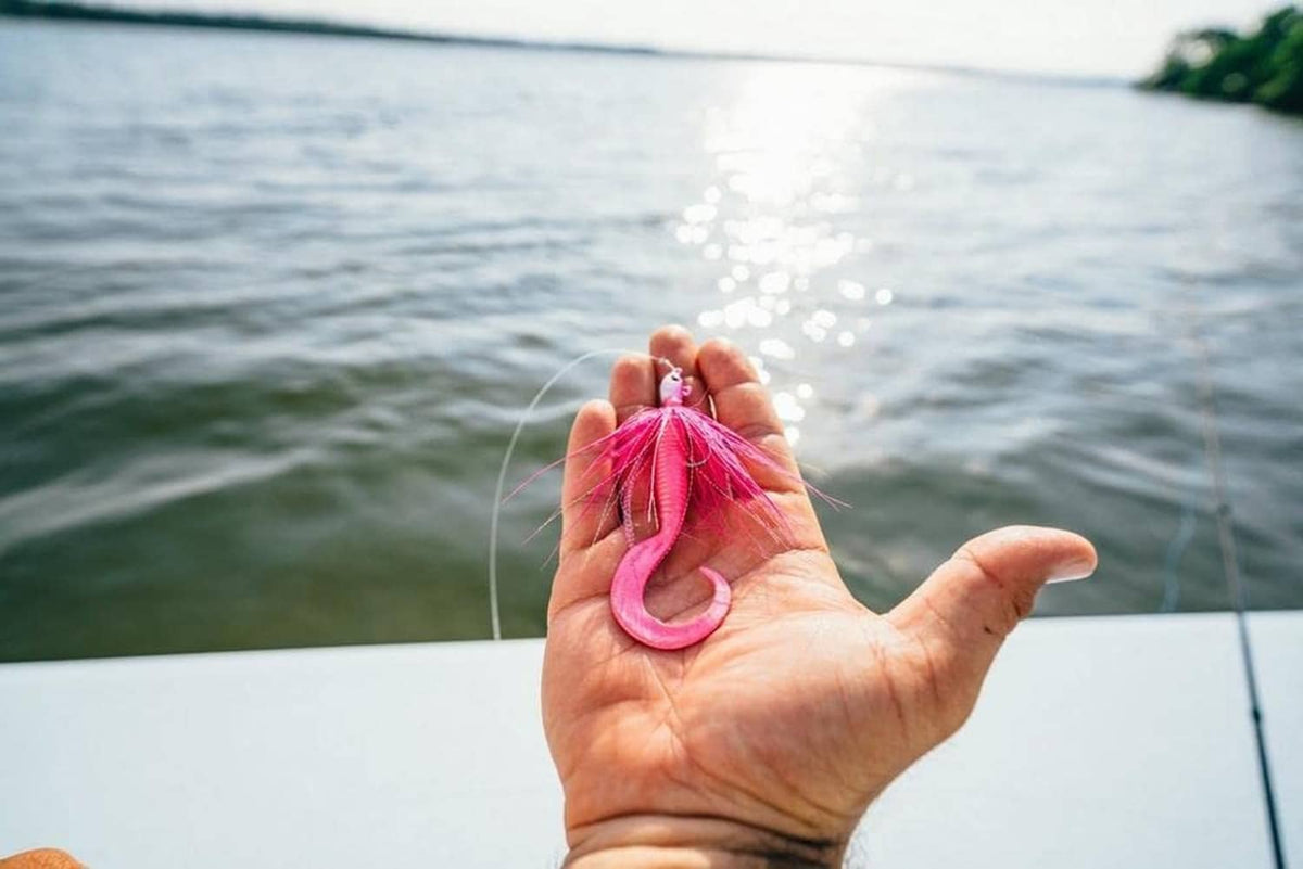 Pink soft bait lure held in hand over the water