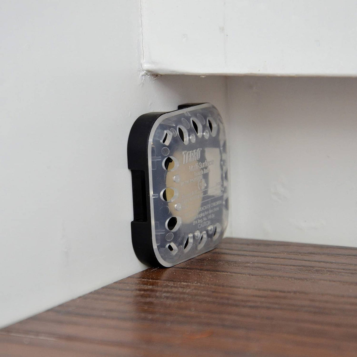 Black roach bait station in corner on wooden floor with see-through top